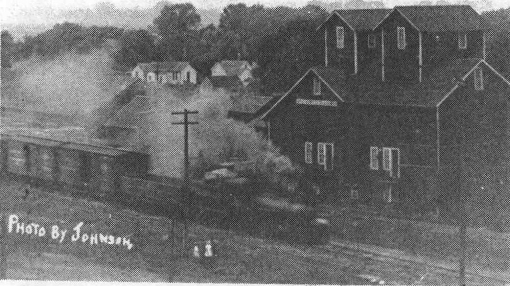 Steam train passing a large wooden grain elevator at Hooper.