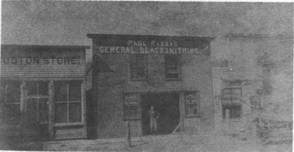 An early blacksmith storefront with a general blacksmithing sign beside another small shop.